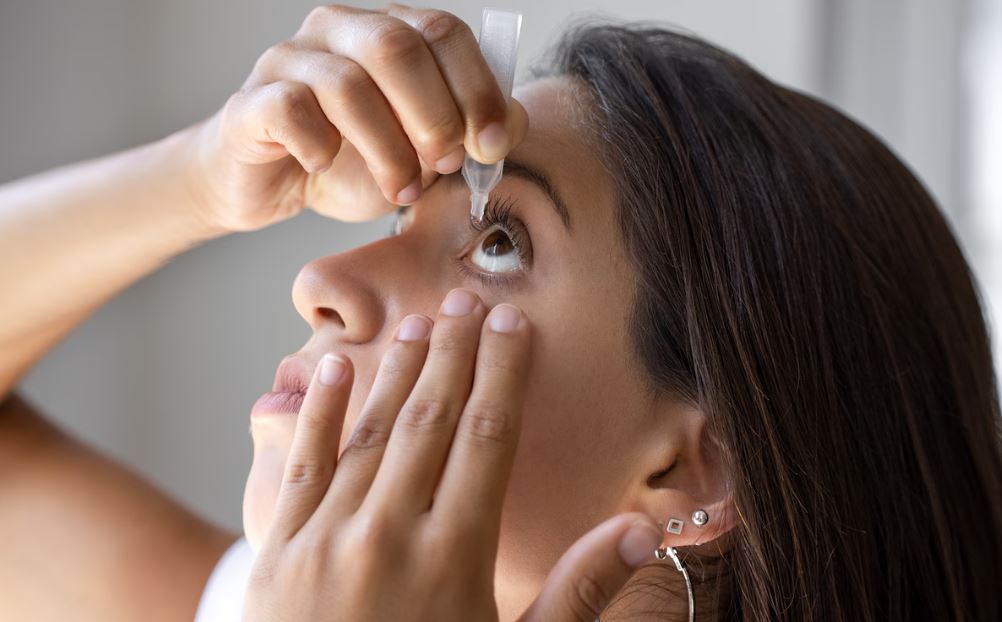 Close-up van een vrouw die een flesje oogdruppels boven haar oog houdt.